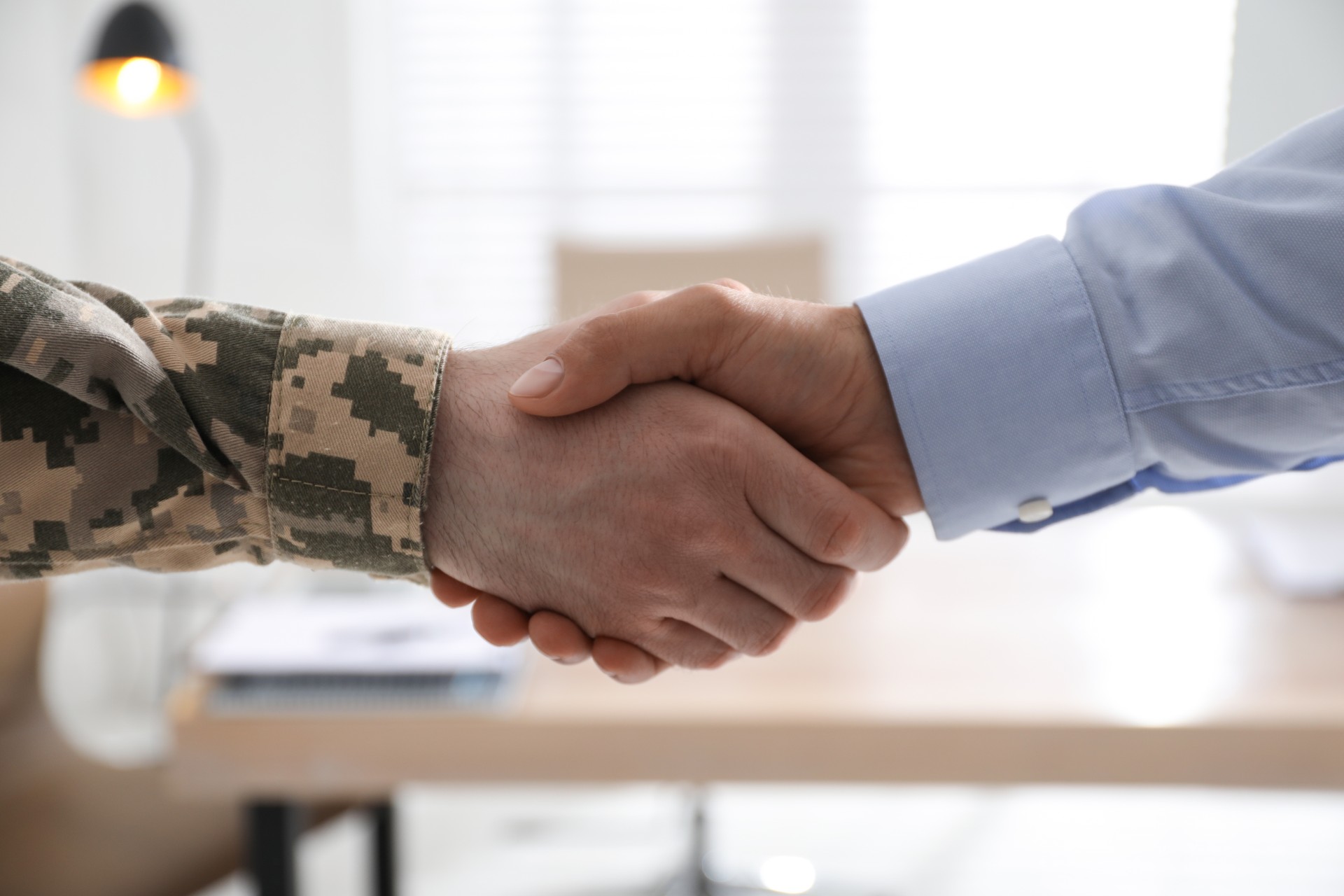 Soldier and businessman shaking hands indoors, closeup